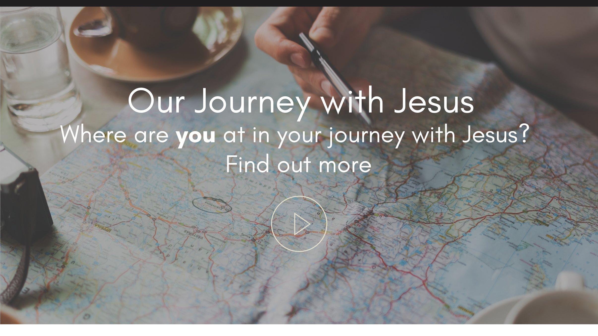 Our Journey with Jesus — where are you at in your journey with Jesus? A hand holding a pen over a paper map on a table with coffee and water, representing planning out a personal journey